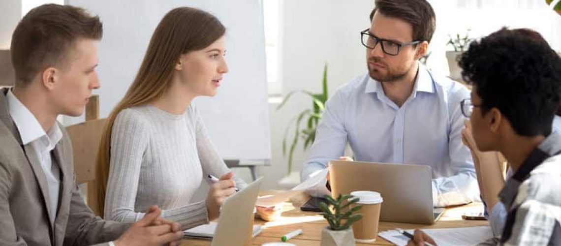 Diverse colleagues listen to coworker talking about new business plan at group meeting, multi ethnic employees brainstorm on project share creative ideas at corporate briefing, team discussion concept