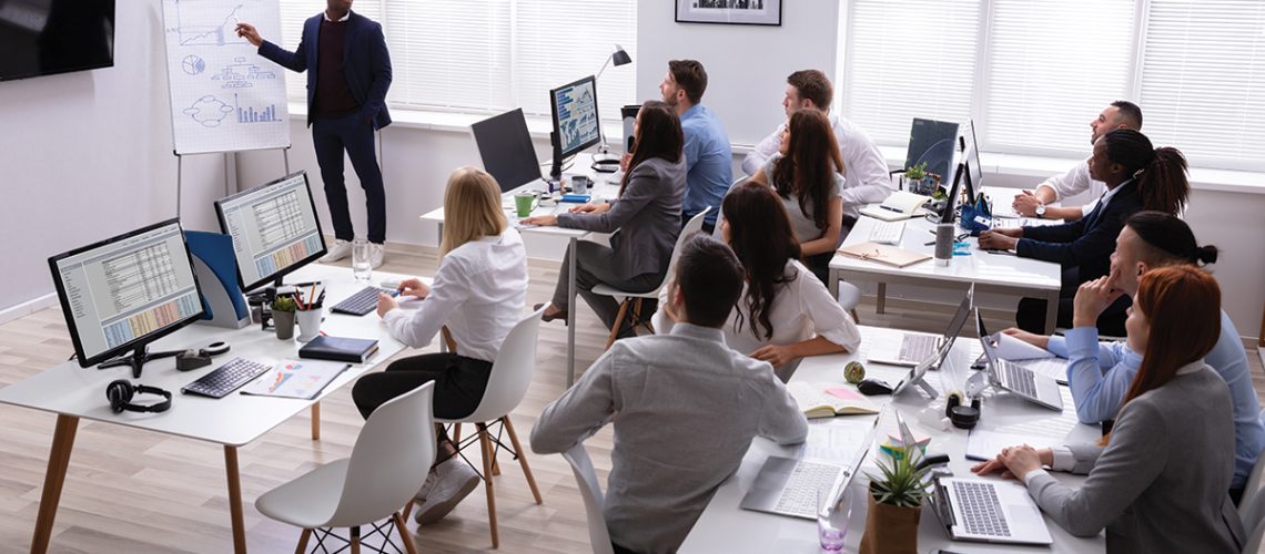 African Businessman Giving Presentation To His Colleagues Sitting On Table With Computers In Office